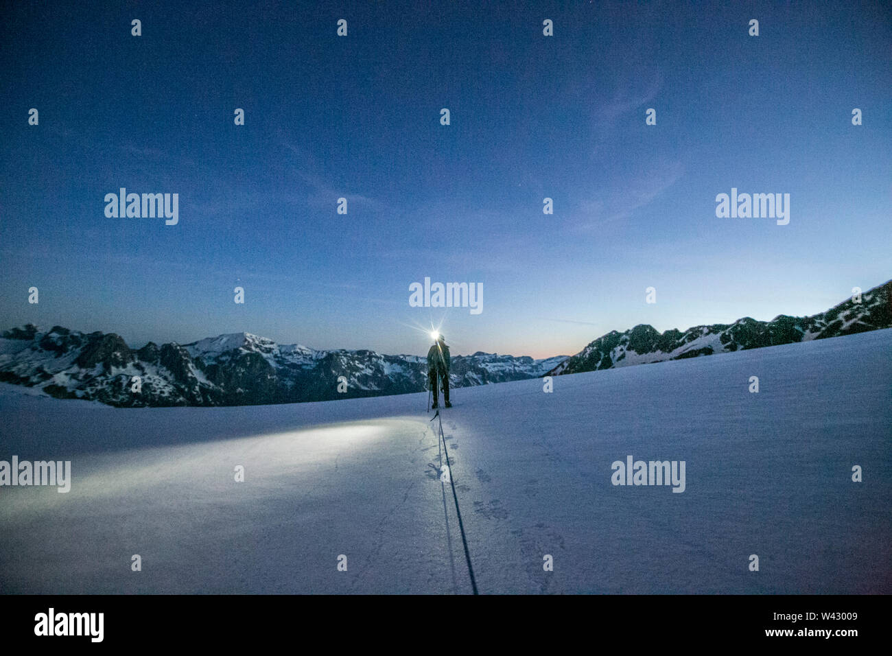 Un alpinista utiliza un proyector para navegar con glaciares del terreno antes del amanecer Foto de stock
