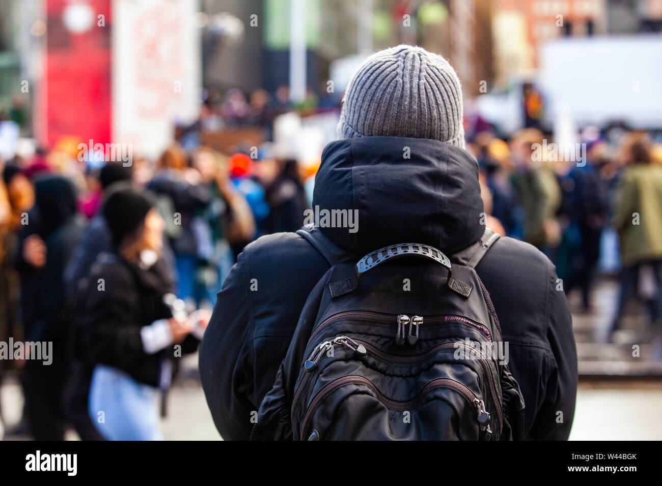 Un hombre que llevaba una mochila es visto desde atrás, como una gran multitud de los ambientalistas se ve borroso en el fondo. Con espacio para copiar Foto de stock