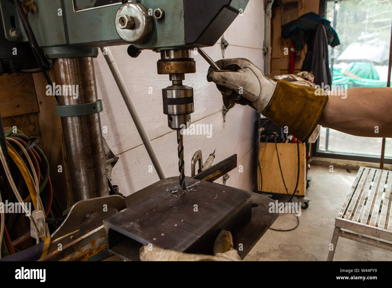 Una vista de cerca de un trabajador metalúrgico operar un taladro de banco  dentro de su taller. Máquina de servicio pesado se usa para perforar un  agujero a través del metal Fotografía