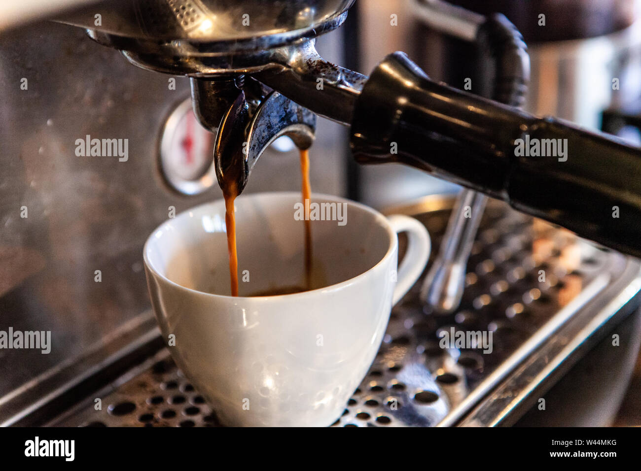 Una vista cercana de un filtro de cafetera de goteo lento en acción,  creando un espresso en una pequeña taza de café molido blanco, frijoles son  filtradas con agua tibia Fotografía de