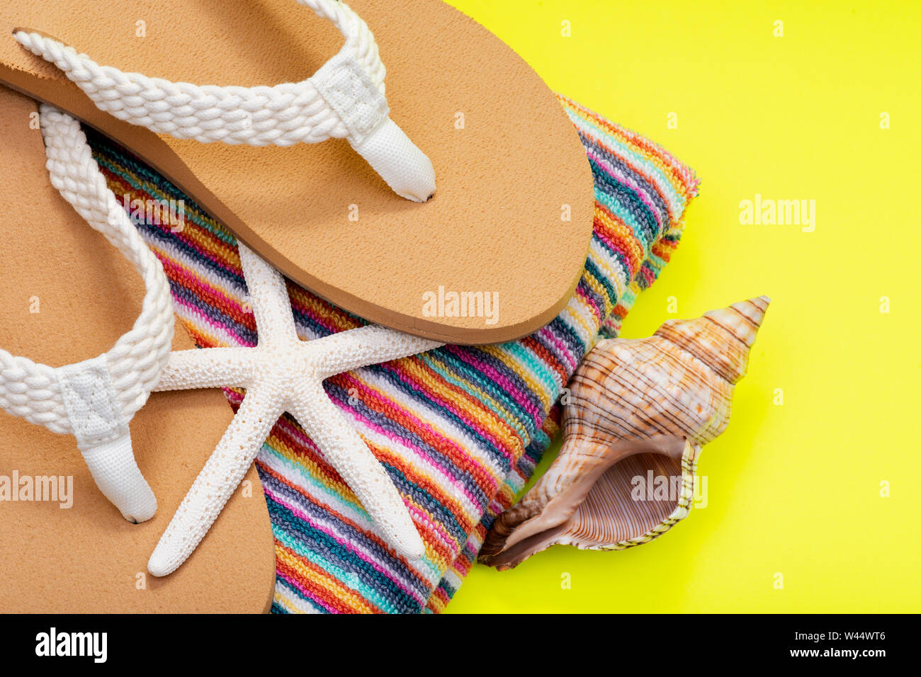 La mujer de color natural Causal chanclas de playa y una toalla de playa de rayas coloridas dedo blanco decorado con estrellas de mar y conchas sobre fondo amarillo Fotografía stock -