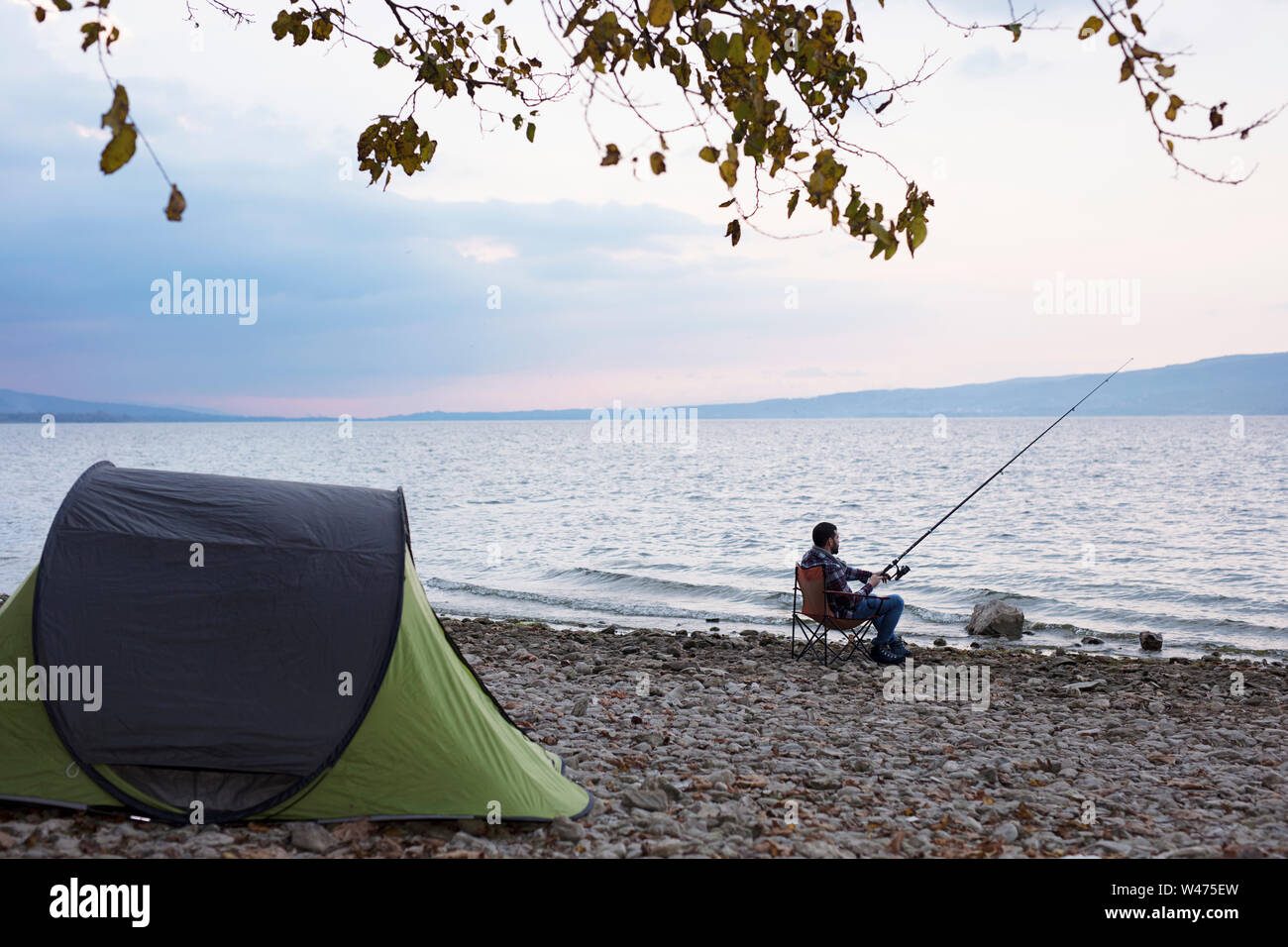 El hombre en el campamento cerca del lago, intentar la pesca Foto de stock