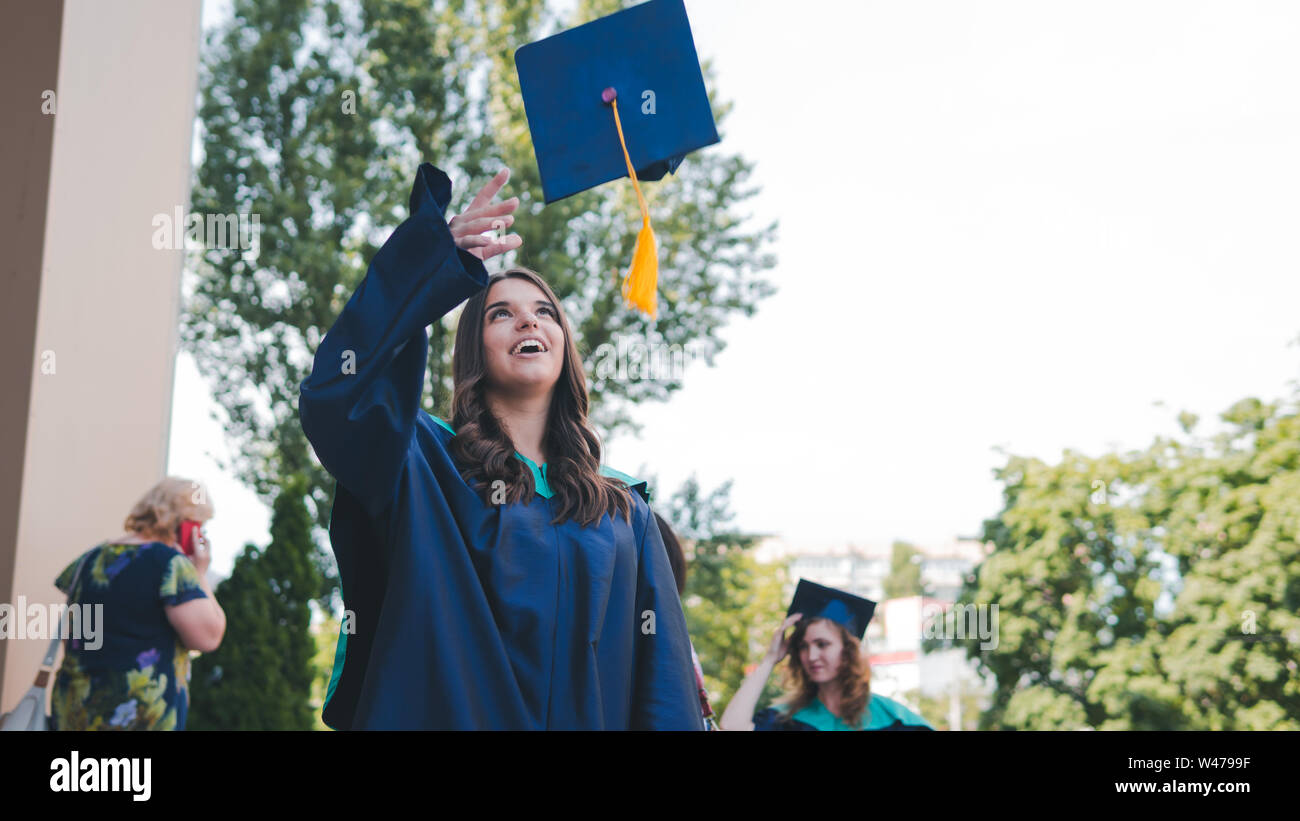 Graduados universitarios arrojando sombreros de graduación en el aire.  Grupo de graduados en la feliz vestidos académica cerca de los edificios de  la universidad. Los jóvenes estudiantes vestido Fotografía de stock -