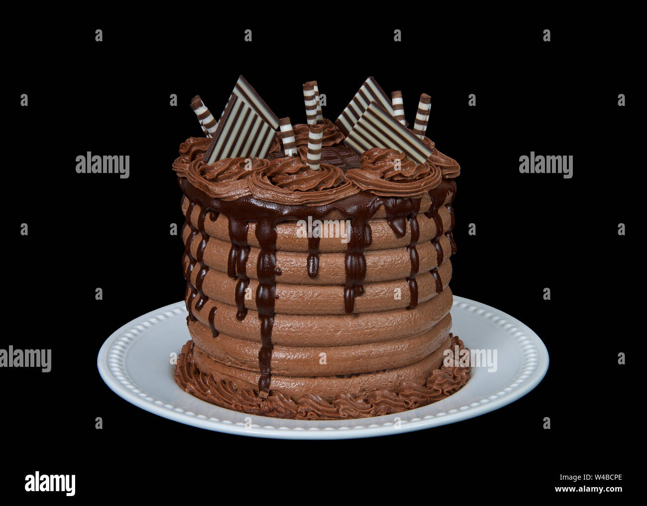 Cerrar sobre toda la tarta de chocolate con ganache de chocolate de goteo hacia abajo los lados y dulces para decorar en la parte superior presenta en pequeñas placas de porcelana blanca, Foto de stock