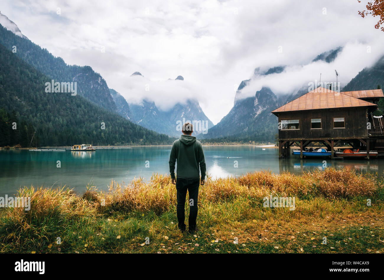 Joven excursionista significa volver a la cámara en la orilla del lago de Dobbiaco o Toblacher en Dolomitas con madera boathouse hut, Italia Foto de stock