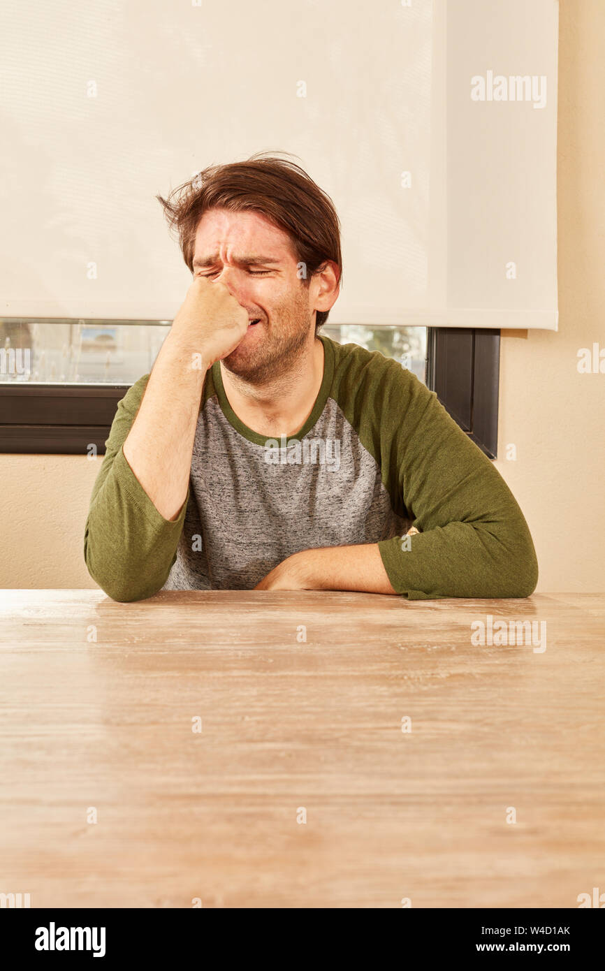 El hombre grita de frustración o desesperación y se sienta solo en la mesa Foto de stock