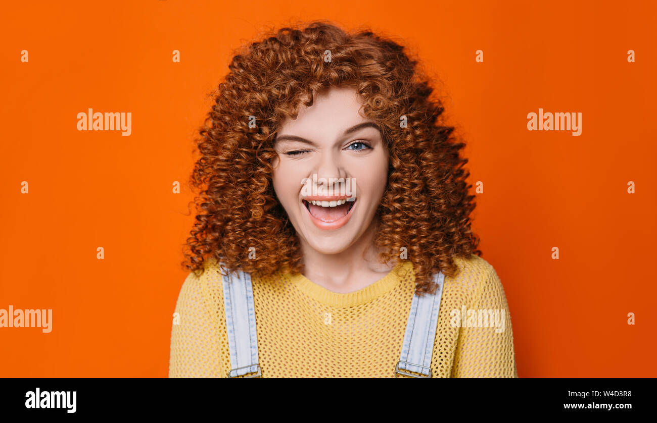 Mujer con pelo rojo rizado un guiño de ojos y boca abierta con grandes sonrisas Foto de stock