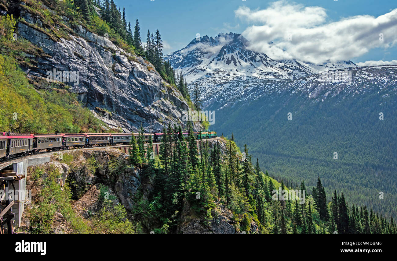 Skagway, Alaska, EE.UU. - Mayo 22, 2019 El White Pass & Yukon Route Railroad viaja a lo largo de los rieles deslizantes debajo de roca en el camino a Skagway. Foto de stock