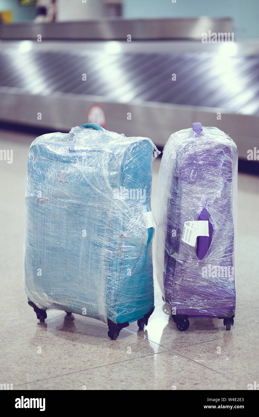 Equipaje en el aeropuerto en el area de reclamo de equipaje en la cinta  transportadora. Dos maletas envueltas en plástico, de pie sobre un  brillante mosaico de piedra, selectiva foc Fotografía de