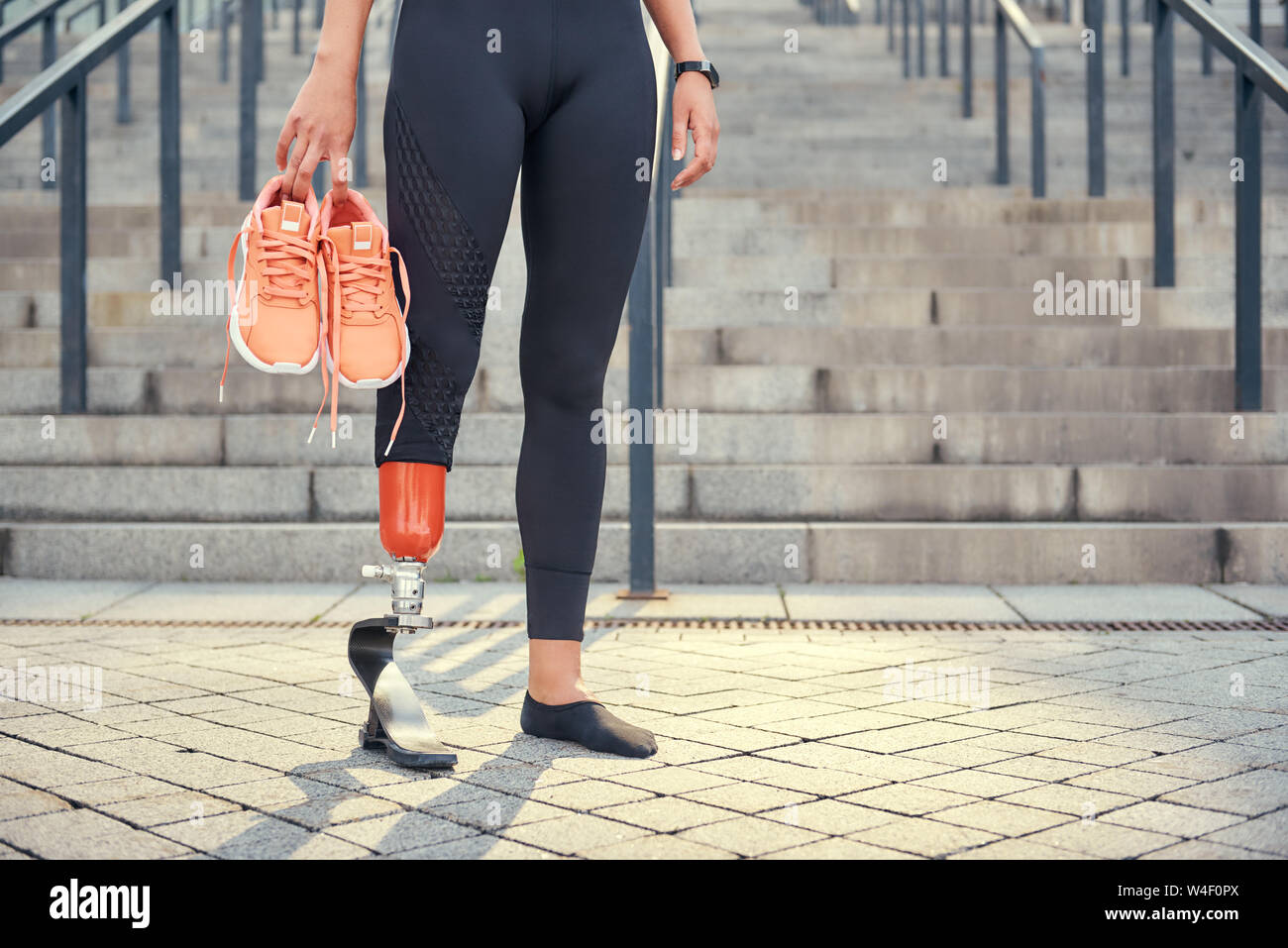 Mantener mi cuerpo sano. Foto recortada de mujer con prótesis de pierna en llevando sus zapatillas naranja mientras está de pie en escaleras exteriores. Deshabilitado el deporte concepto Fotografía