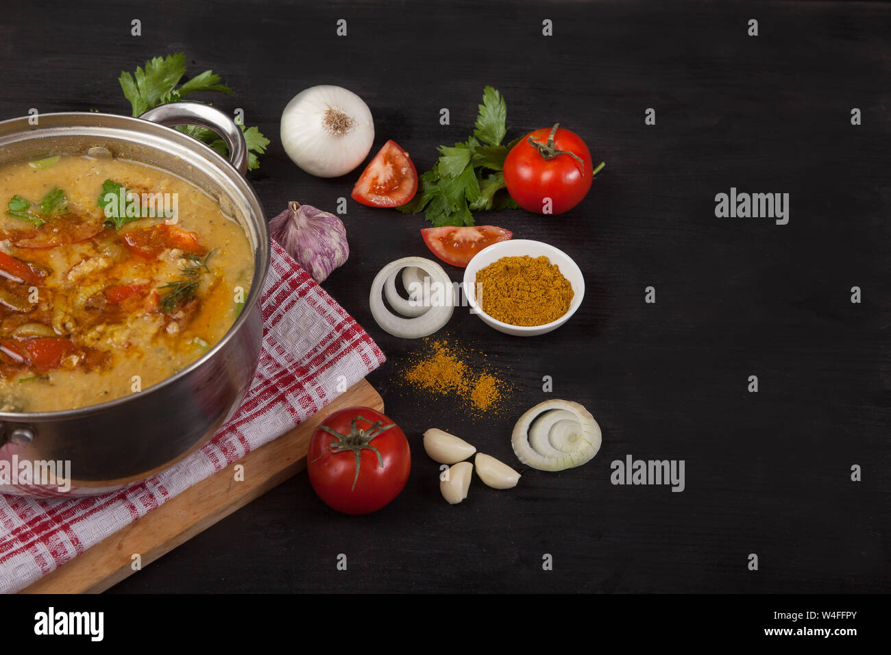 Una sopa de lentejas rojas cazuela se erige sobre una servilleta en un fondo negro. Cerca de la cebolla, el ajo y las especias. Copiar spaes Foto de stock