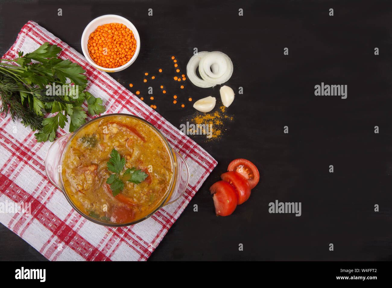 Sopa de Lentejas rojas con tomates, cebollas, ajo, hierbas y especias en una placa de vidrio de pie sobre un mantel sobre un fondo negro. Copiar spaes Foto de stock