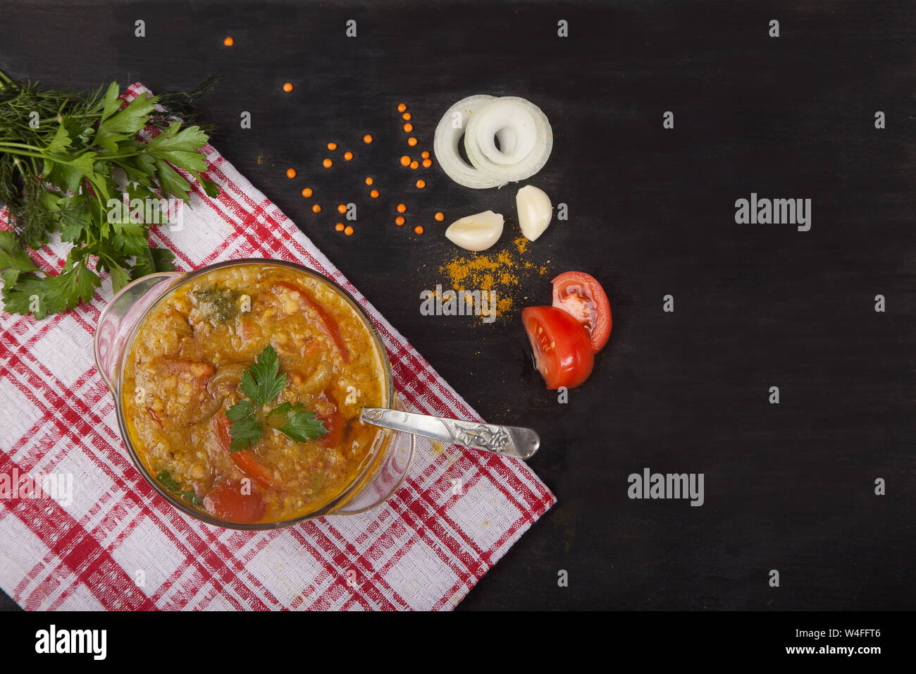 Sopa de Lentejas rojas con tomates, cebollas, ajo y especias en un recipiente de cristal con una cuchara de pie sobre un mantel sobre un fondo negro. Copiar spaes Foto de stock