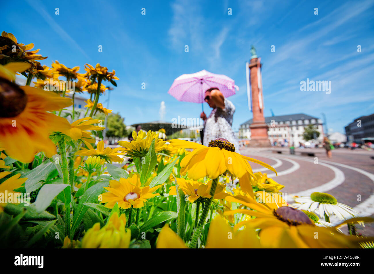 Darmstadt, Alemania. 23 de julio de 2019. Una mujer con sombrilla camina pasado una flor calada. En el fondo es la Darmstadt hito de la "Lange Ludwig'. Crédito: Andreas Arnold/dpa/Alamy Live News Foto de stock