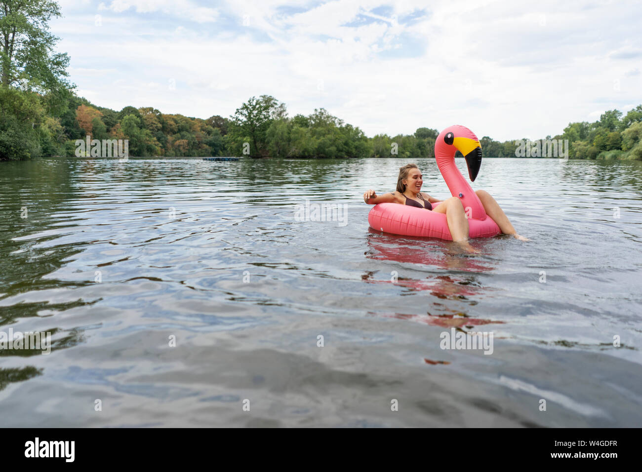 Mujer joven flotando sobre un lago en una llanta flotante del flamenco rosado Foto de stock