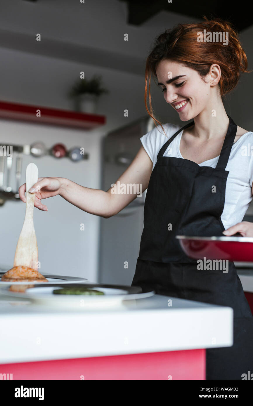 Mujer sonriente colocando el buñuelo de paté en su cocina Foto de stock