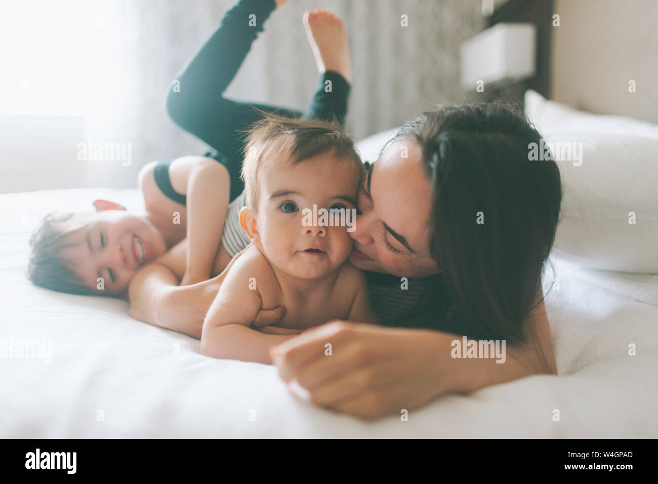 Madre y dos muchachos caricias en la cama en casa Foto de stock