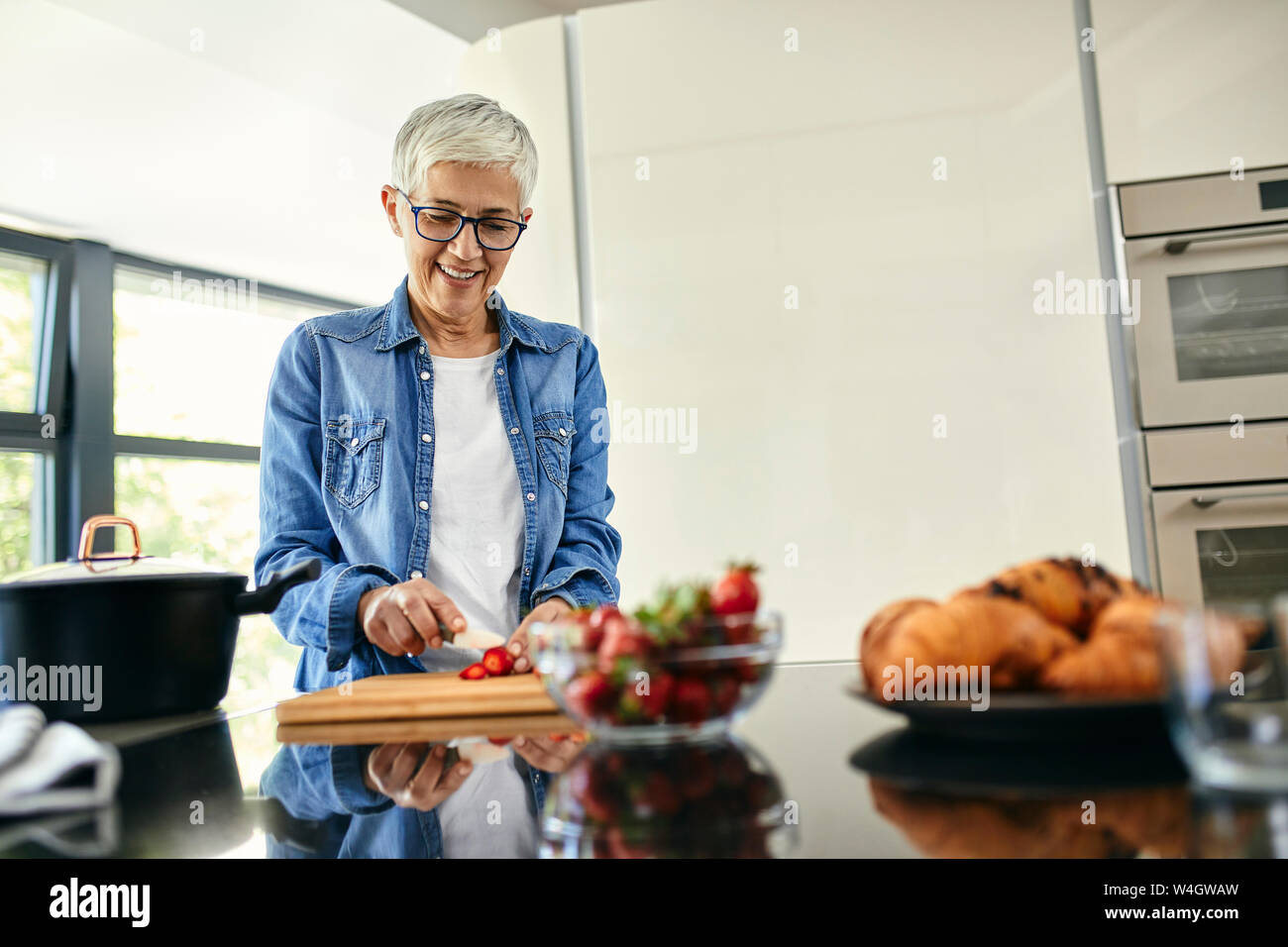 Mujer de pie senior en la cocina, picar las fresas Foto de stock