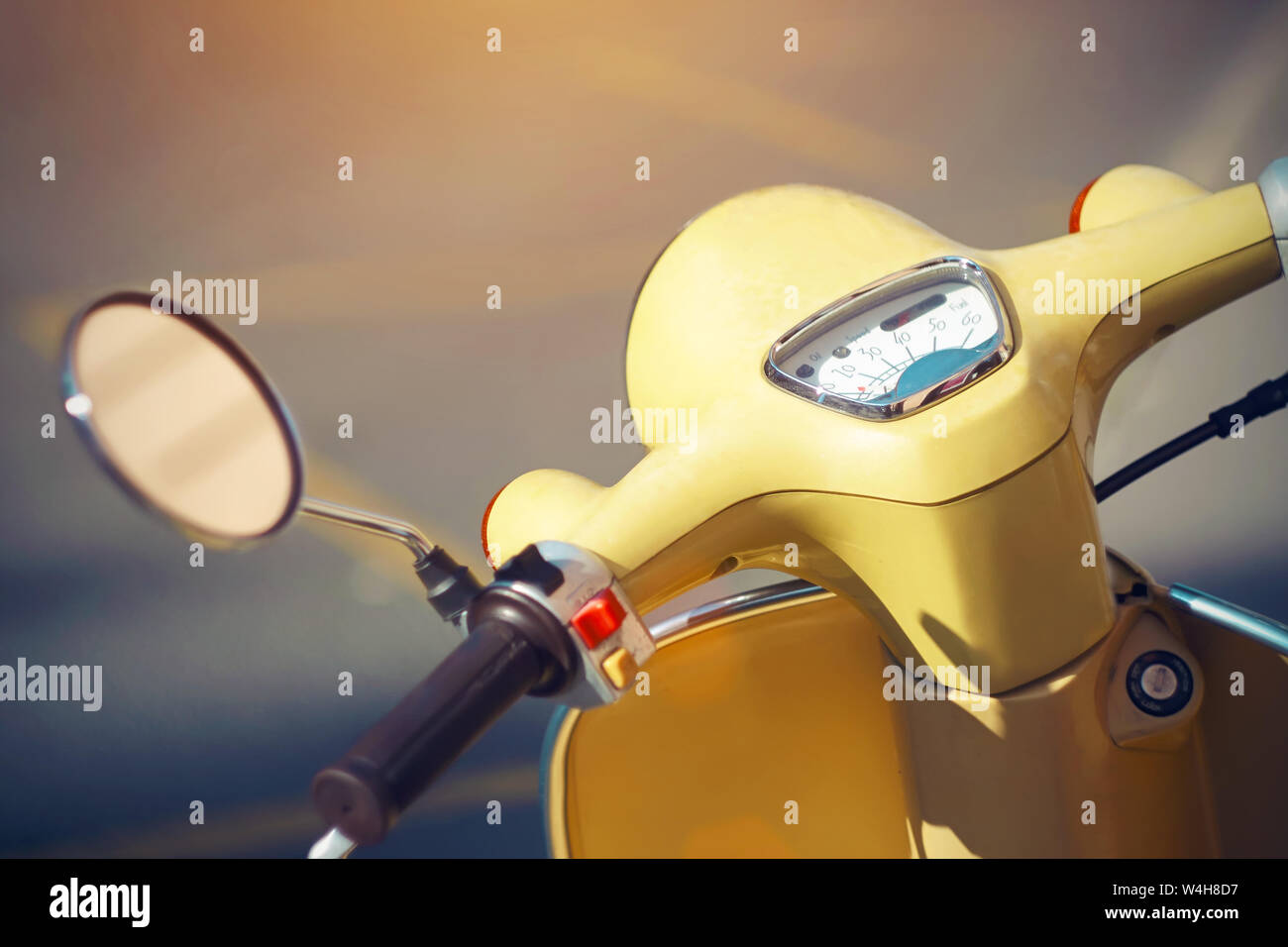 Al volante de un ciclomotor amarillo vintage con un retrovisor y un velocímetro, que se encuentra en el camino con marcas amarillas, iluminada por Foto de stock