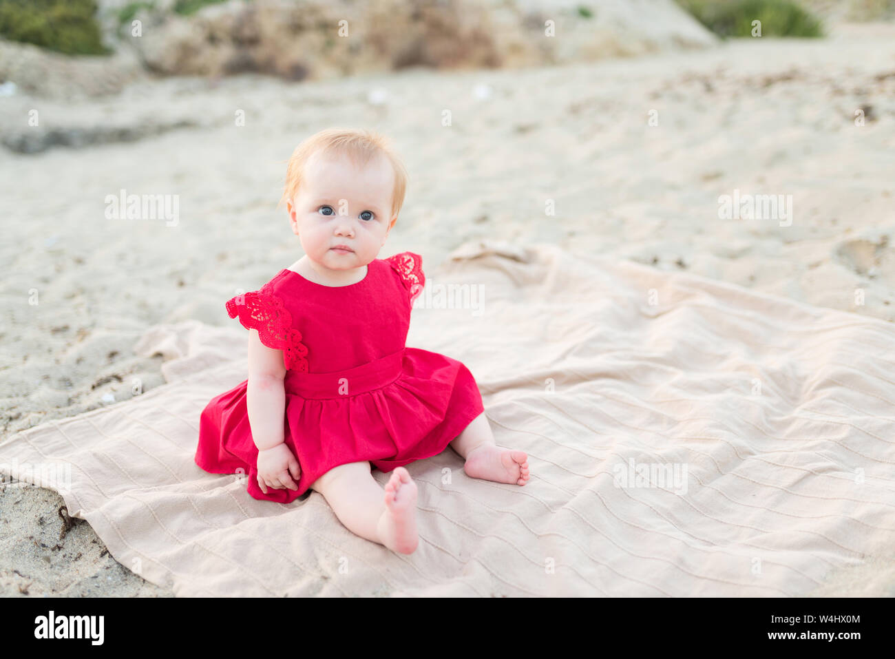 Lindo bebé niña en un vestido sentado y jugando en la playa arena de - Alamy