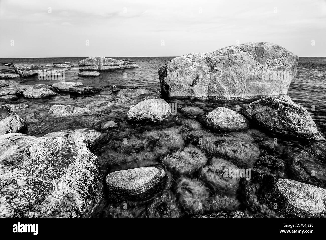 Hermosa enormes piedras en el mar con pequeñas piedras bajo el agua cubiertos de algas verdes en el Golfo de Finlandia. En blanco y negro. Foto de stock
