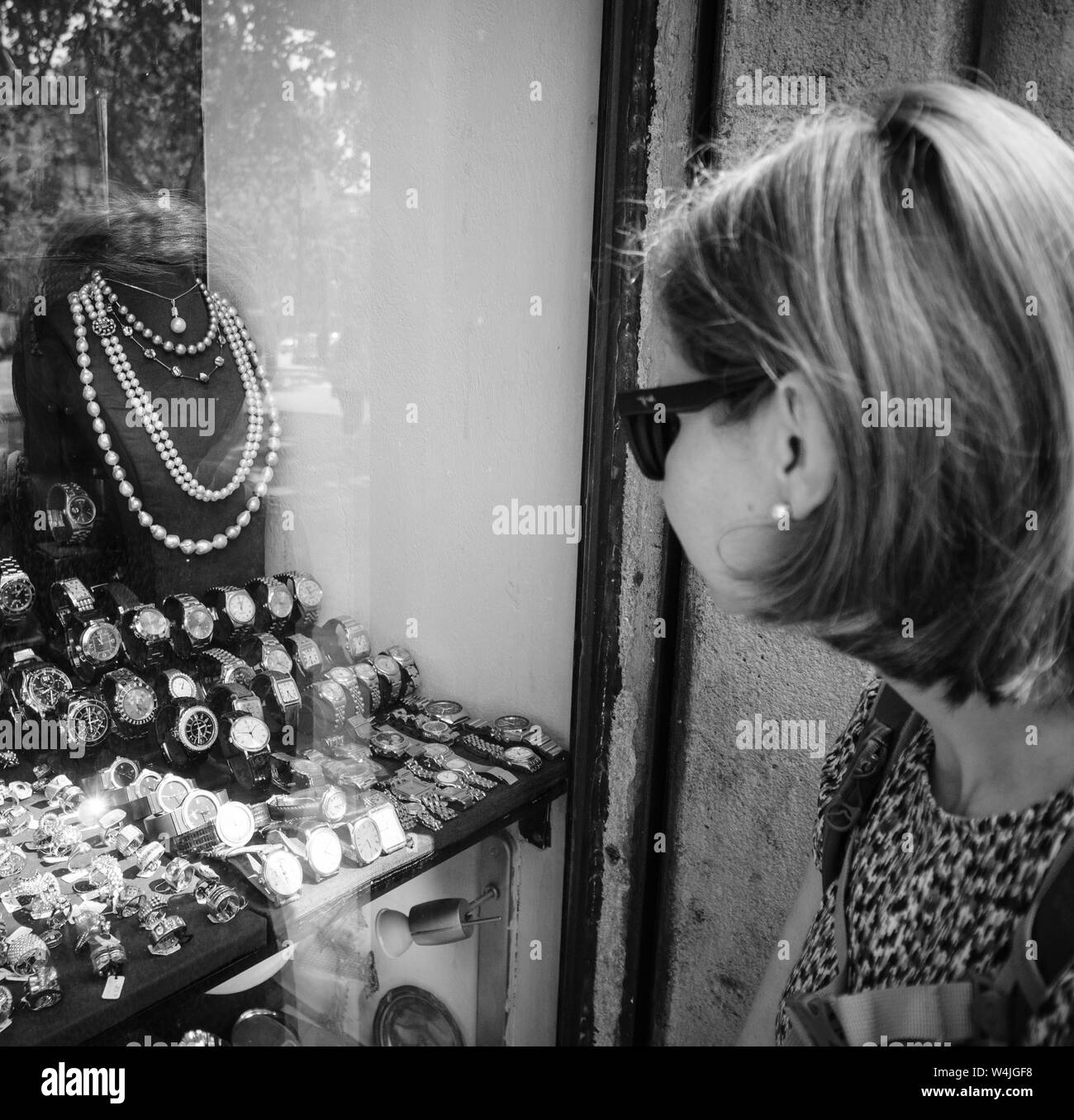 Barcelona, España - Jun 1, 2018: turista elegante mujer mirando al frente  la ventana de exhibición en el centro de joyería en ciudad española  eligiendo anillos, aretes, broches, perlas y diamantes imagen