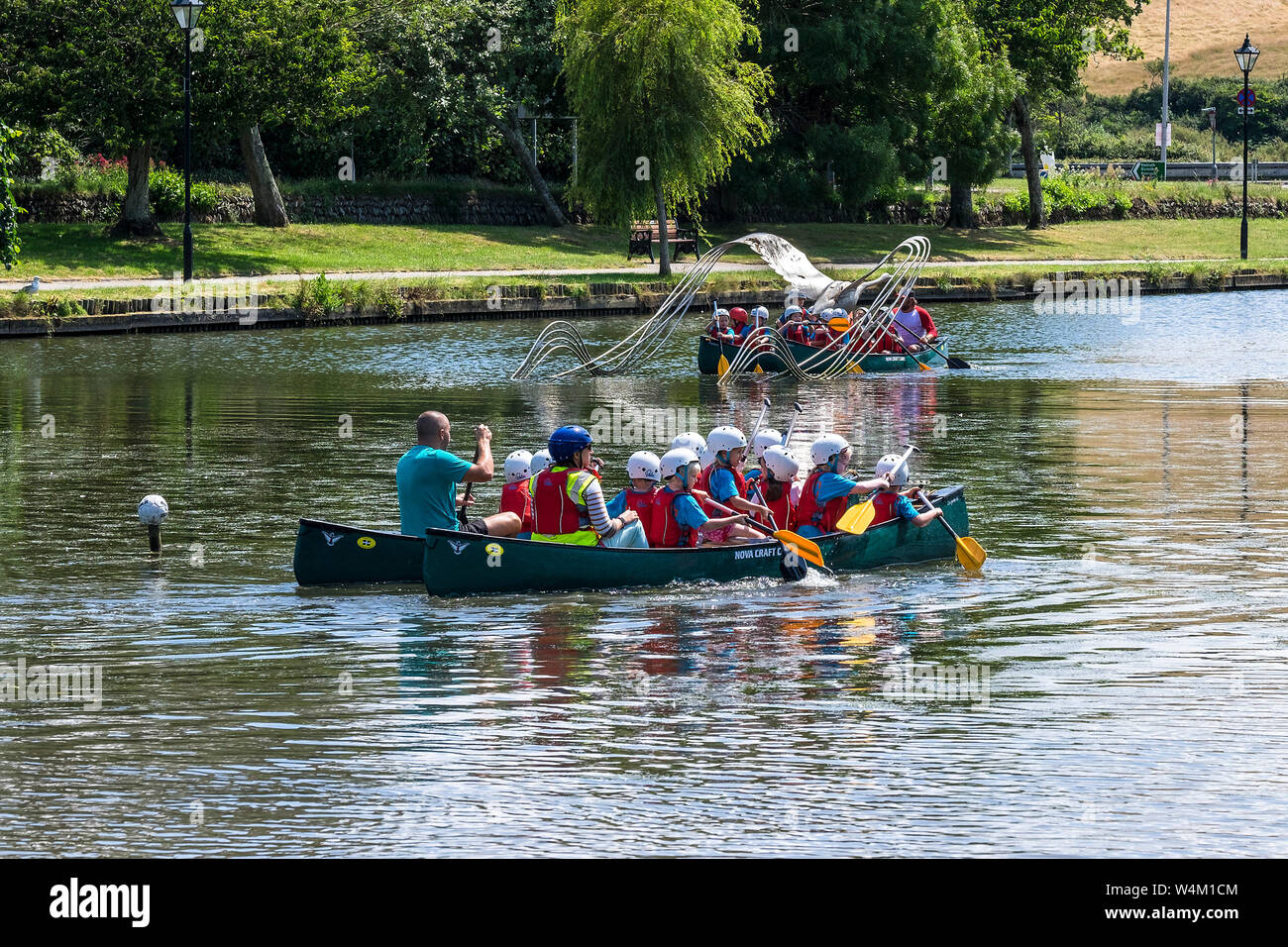 Los alumnos de la escuela primaria de actividad de ocio al aire libre disfrutando de una lección como se divierten canotaje en el lago con botes, Jardines Trenance en Newquay en Cornualles. Foto de stock
