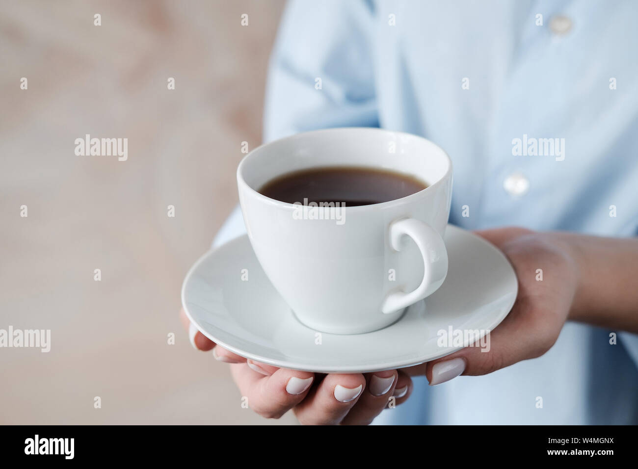 Mujer sosteniendo una taza de café. Manos femeninas con taza de té negro sobre fondo de color beige. Cerrar Foto de stock