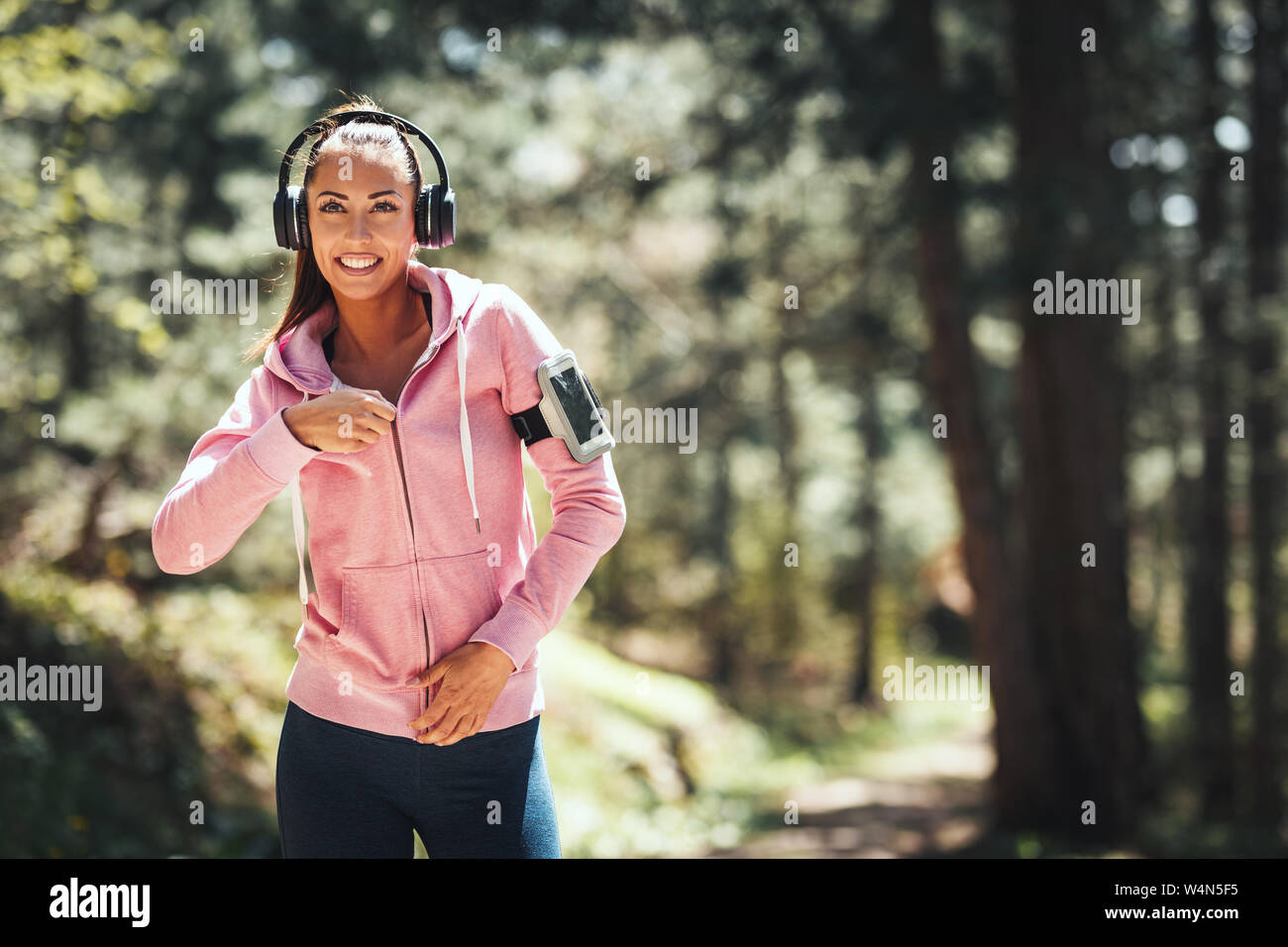 Feliz mujer, vistiendo ropa deportiva, con auriculares en su cabeza está  caminando por un sendero de la selva soleados, disfrutando del paisaje  entre los árboles Fotografía de stock - Alamy