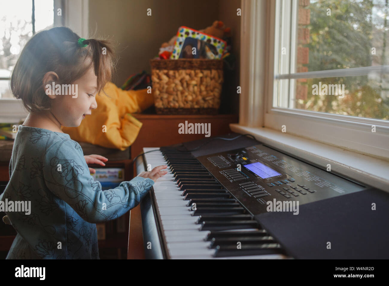 Retrato de un niño pequeño y lindo tocando el piano en frente de una ventana. Foto de stock