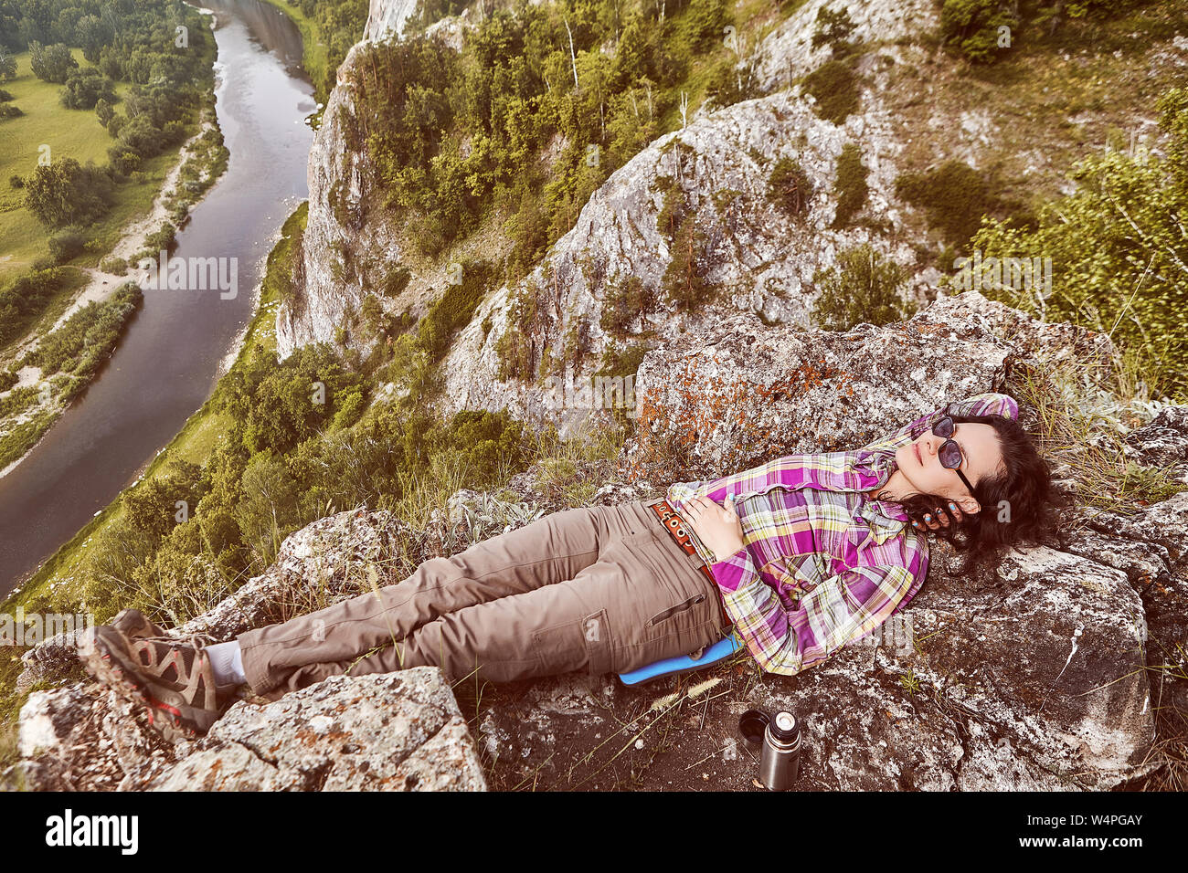 El turismo ecológico en las montañas, una hermosa mujer caucásica descansa en la cima de una montaña, encima de un tranquilo río. Foto de stock