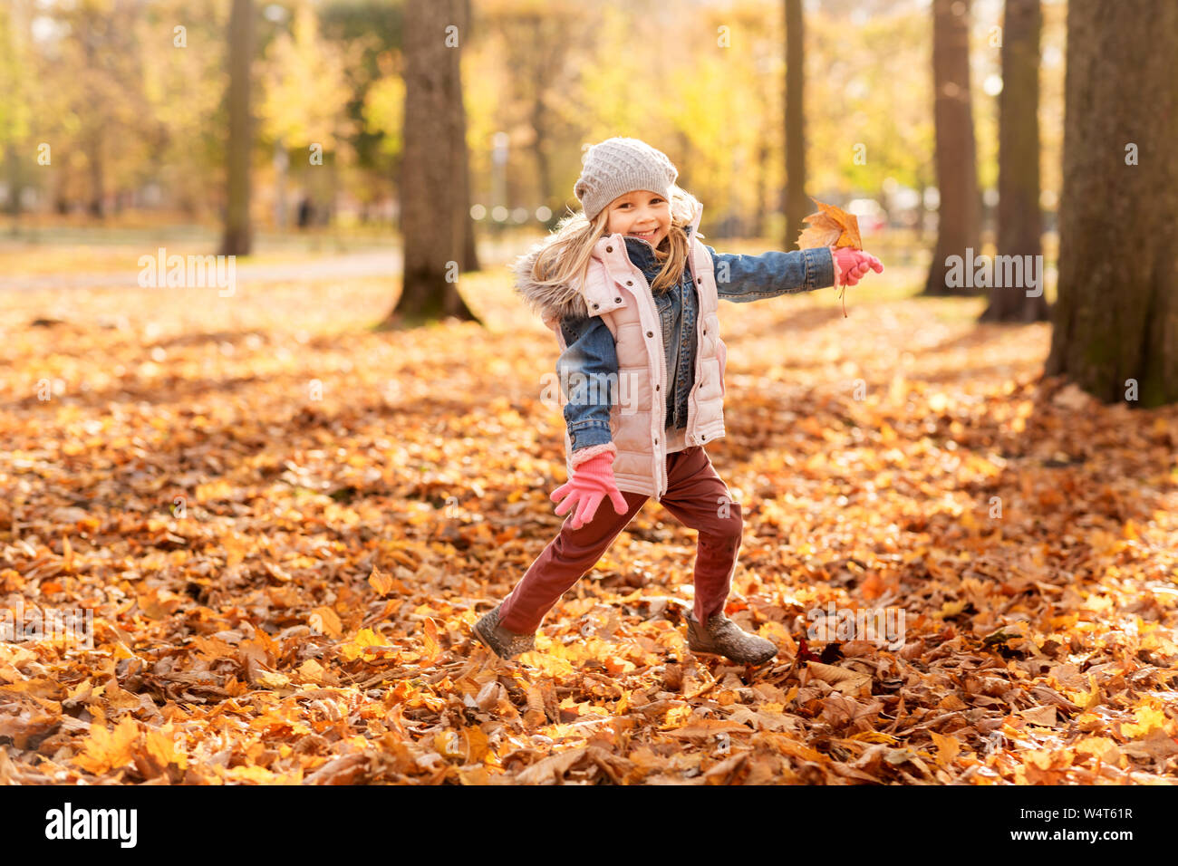 Feliz chica corriendo con maple leaf en otoño park Foto de stock