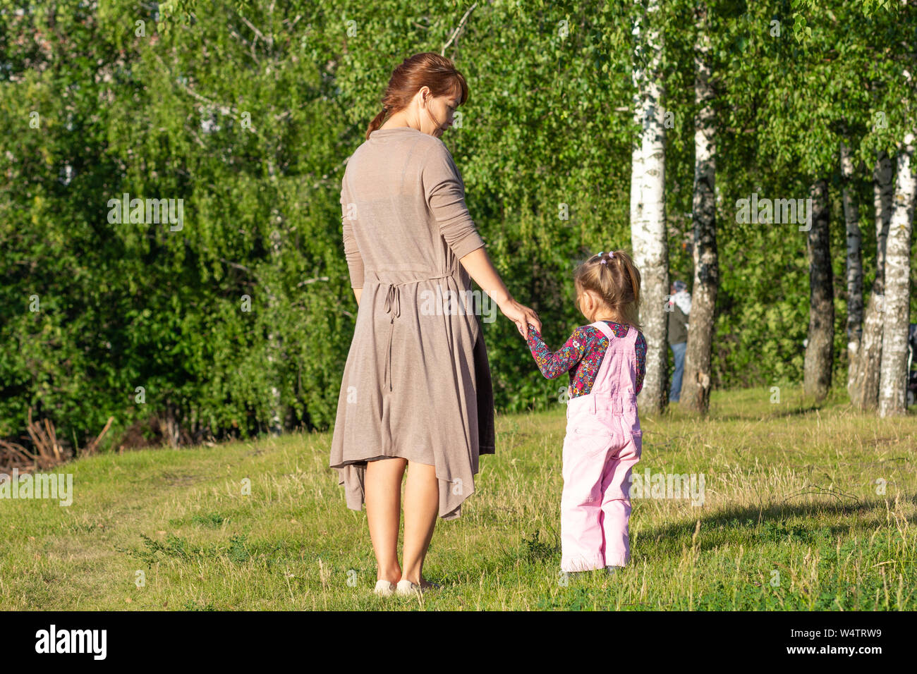 Espaldas de mujer de mediana edad y niños tomados de las manos en el parque con árboles de verano Foto de stock