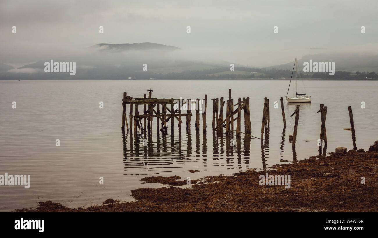 El antiguo muelle de madera arruinada, con las montañas detrás en un día brumoso - Port Bannatyne, Isla de Bute, Escocia Foto de stock