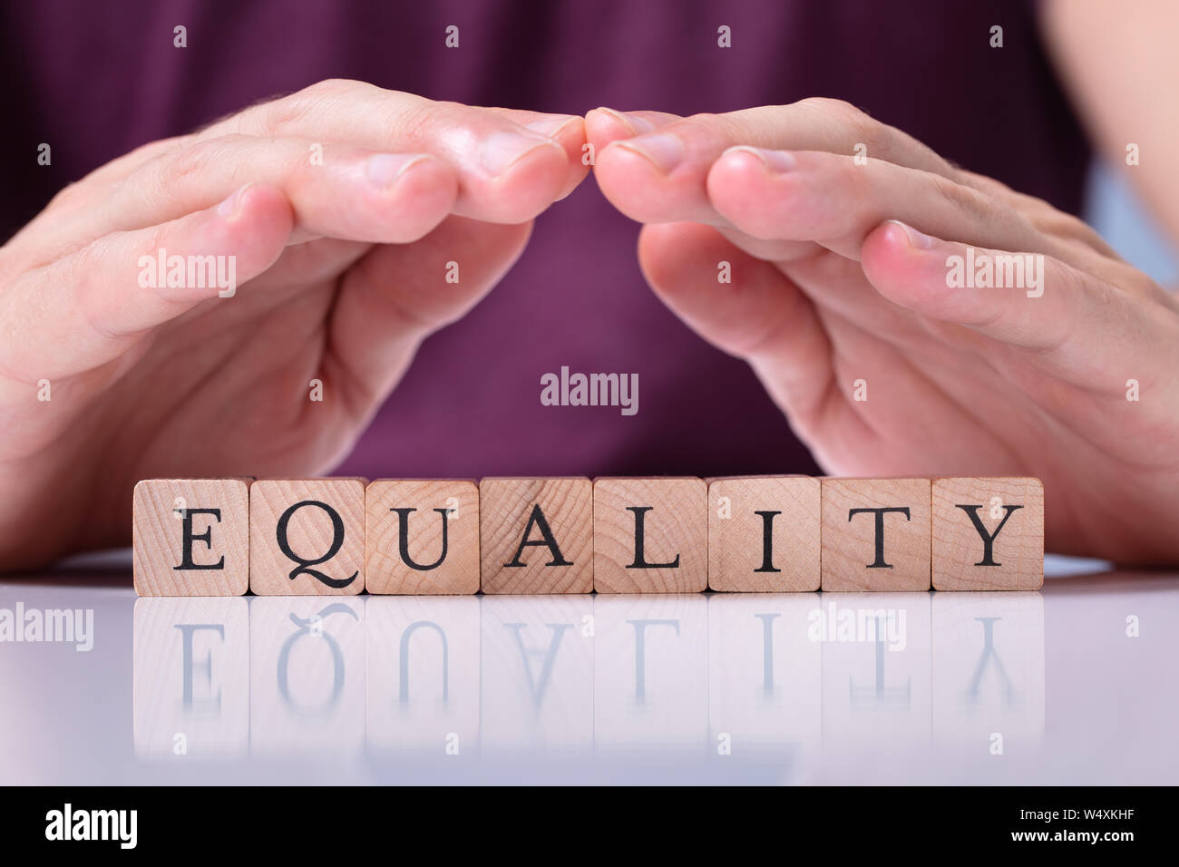 Close-up de la mano del hombre proteger la igualdad palabra sobre bloques de madera sobre mesa reflectante Foto de stock