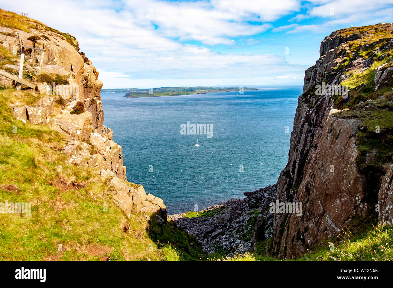 Irlanda del Norte, Reino Unido. Fragmento del acantilado de cabeza justo en la esquina nordeste del Condado de Antrim con la vista lejana de Rathlin Island, un velero y Atl Foto de stock