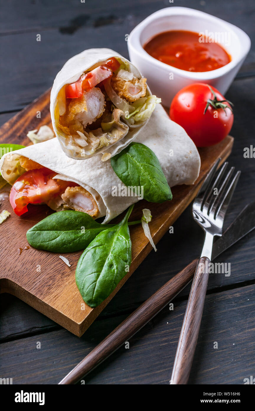 En primer plano se envuelve con tortillas de camarones fritos, lechuga y tomate, sobre una tabla de cortar de madera. La comida saludable. Disparo vertical Foto de stock