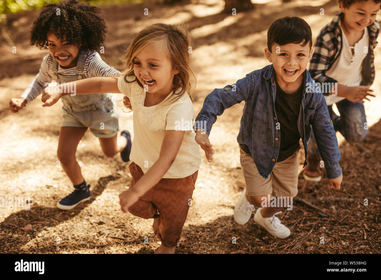 Adorable niños corriendo cuesta arriba en un parque. Grupo de niños jugando juntos en el bosque. Foto de stock