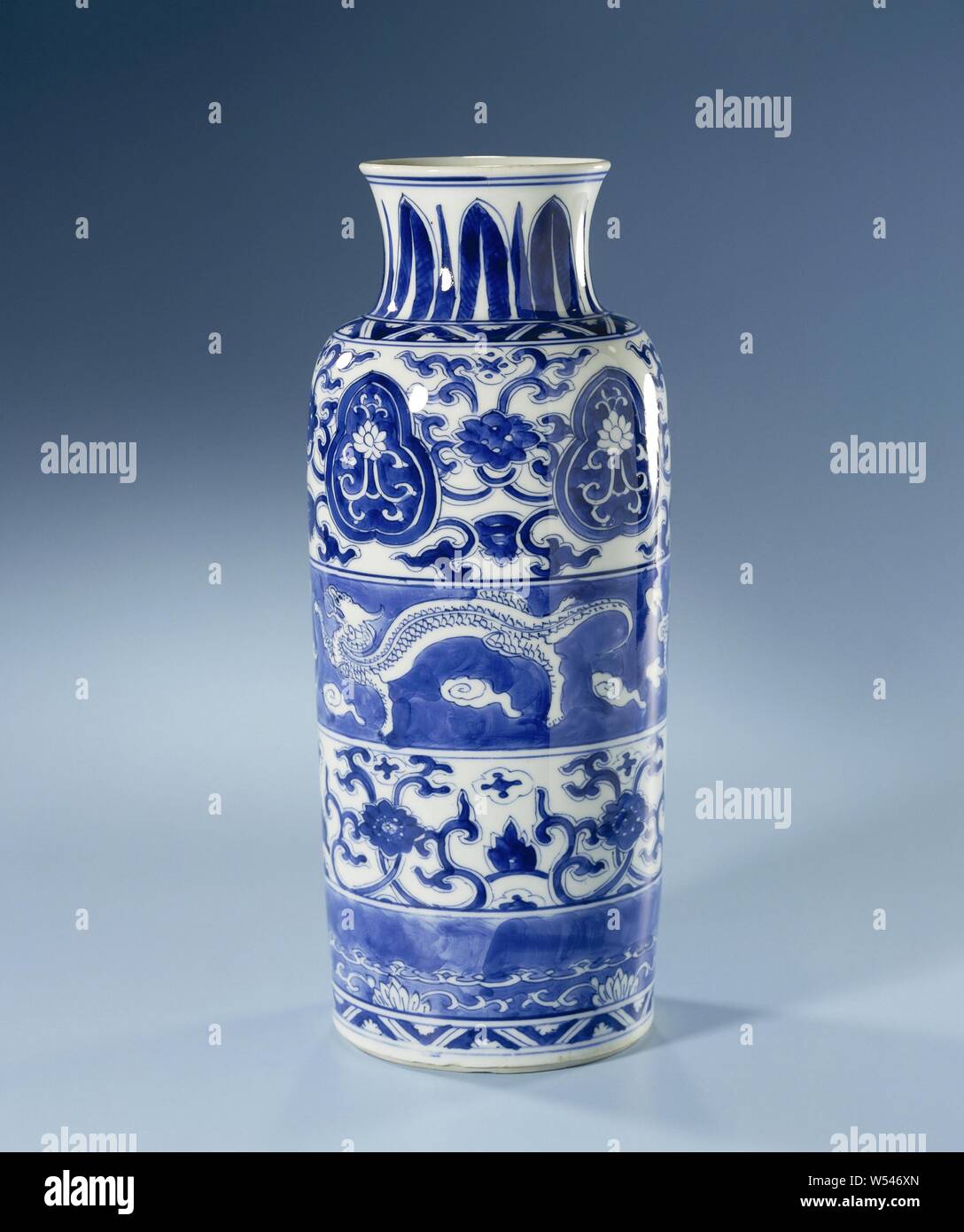 Jarrón cilíndrico con dragones y pergaminos, florales Jarrón cilíndrico de porcelana con una amplia propagación de cuello, pintado de azul underglaze. El vientre está dividido en cuatro bandas anchas de abajo a arriba: una banda con rebajes de lotus vides, uno con flor de vides, uno con dos chilongs (encuestados dragon) con un hongo (lingzhi) entre nubes y uno con flor de vides interrumpida por un lotus rebajada vid en una orla lobuladas. Sobre el hombro y sobre el pie de una banda con un zigzag con flores. El cuello con pie, señaló motivos de hojas. Azul y blanco, Jean Theodore Royer, anónimo Foto de stock