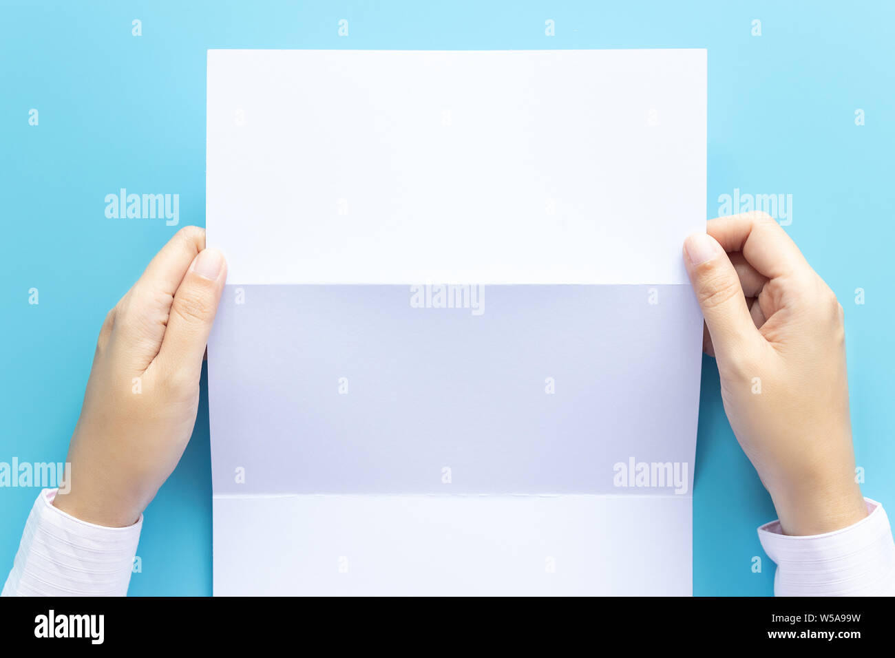 Mano sujetando el papel blanco para carta ficticia, aislado sobre fondo azul, con copia espacio. Foto de estudio Foto de stock