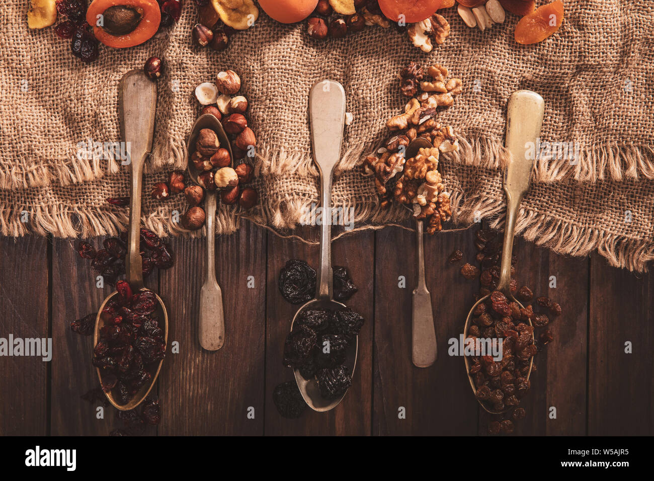Las frutas secas y las nueces dispuestas en una cuchara, tela y una vieja mesa. Composición horizontal en el viejo estilo. Foto de stock