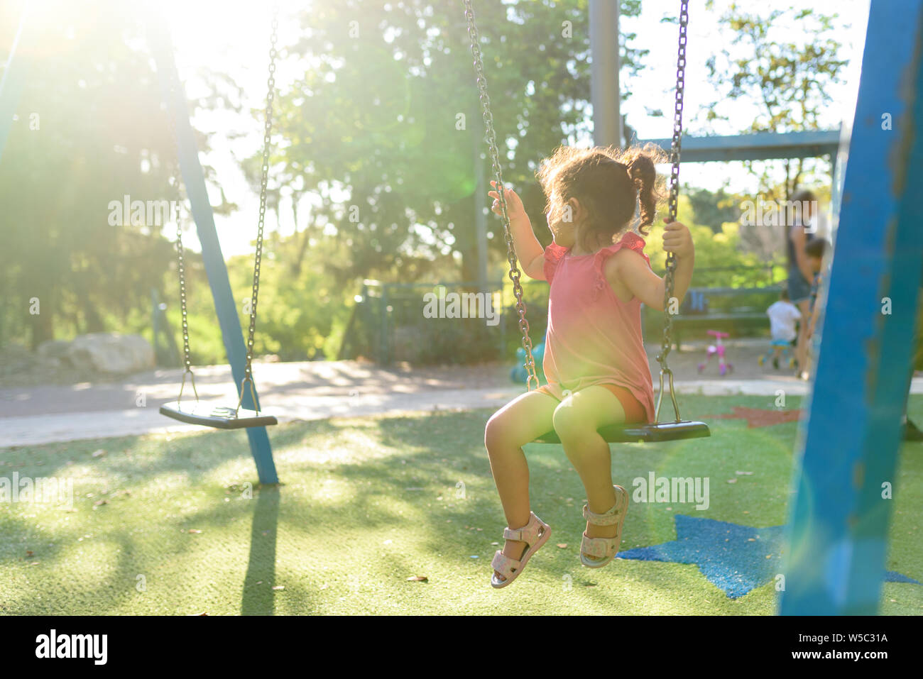 Niño feliz chica riendo y balancearse en un columpio en el patio en verano. Foto de stock