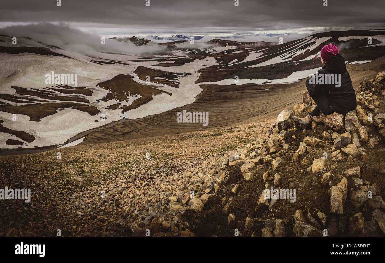 Mujer mirando snowy mountainscape sat, Laugavegur trail Islandia Foto de stock