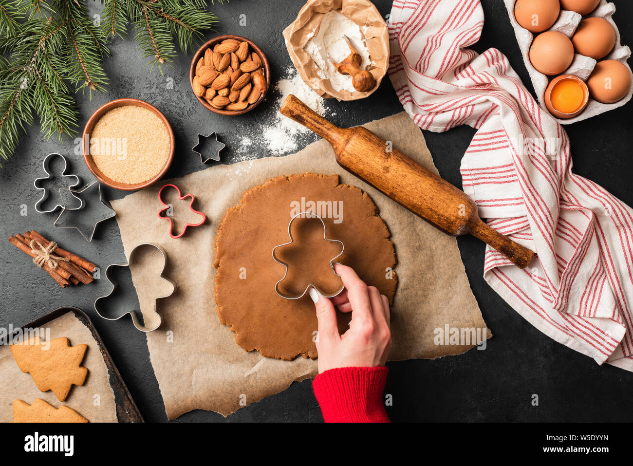 Navidad galletas de jengibre preparación sobre la tabla de pizarra negra. Mano de mujer haciendo galletas festivas con especias Foto de stock
