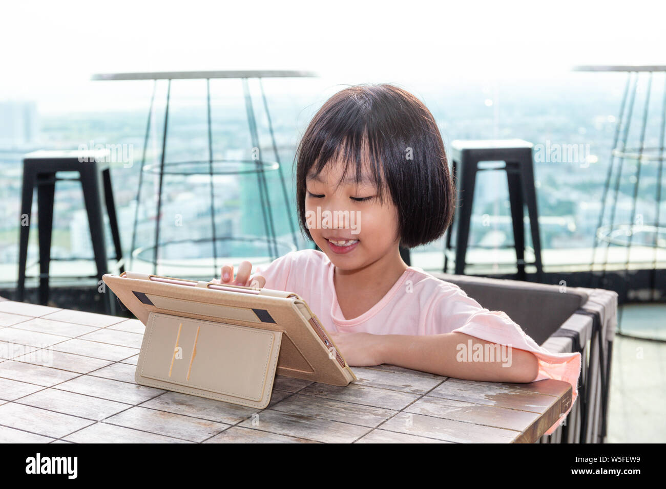 Niña China Asia jugando con la tableta en la cafetería al aire libre Foto de stock