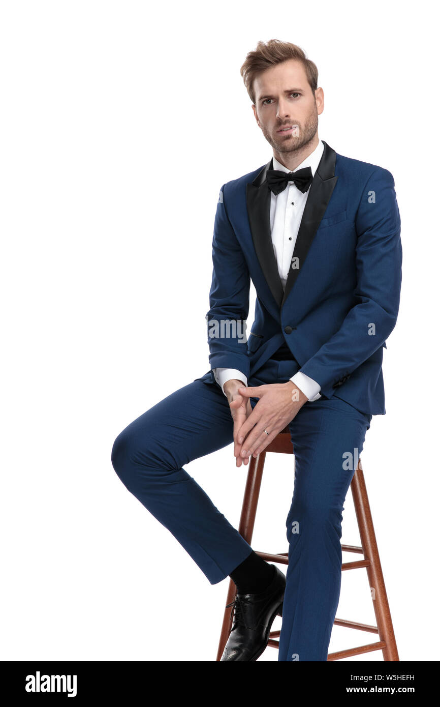 Moda hombre en traje azul sentado en heces manteniendo sus manos sobre  fondo blanco Fotografía de stock - Alamy