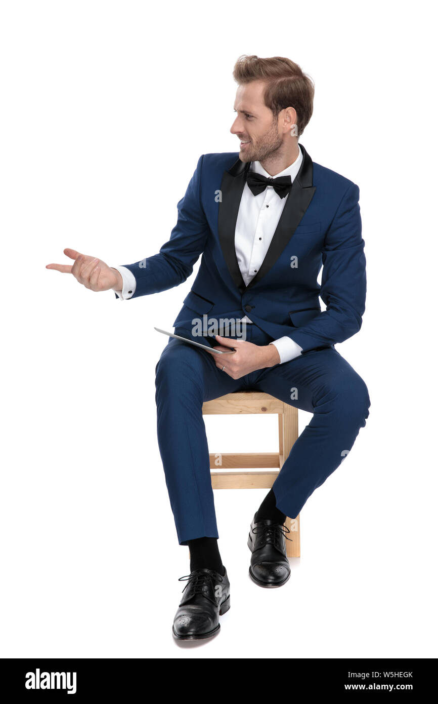 Guapo en traje azul interrogatorio mientras está sentado y la celebración de un bloc de notas en su mano sobre fondo blanco. Foto de stock