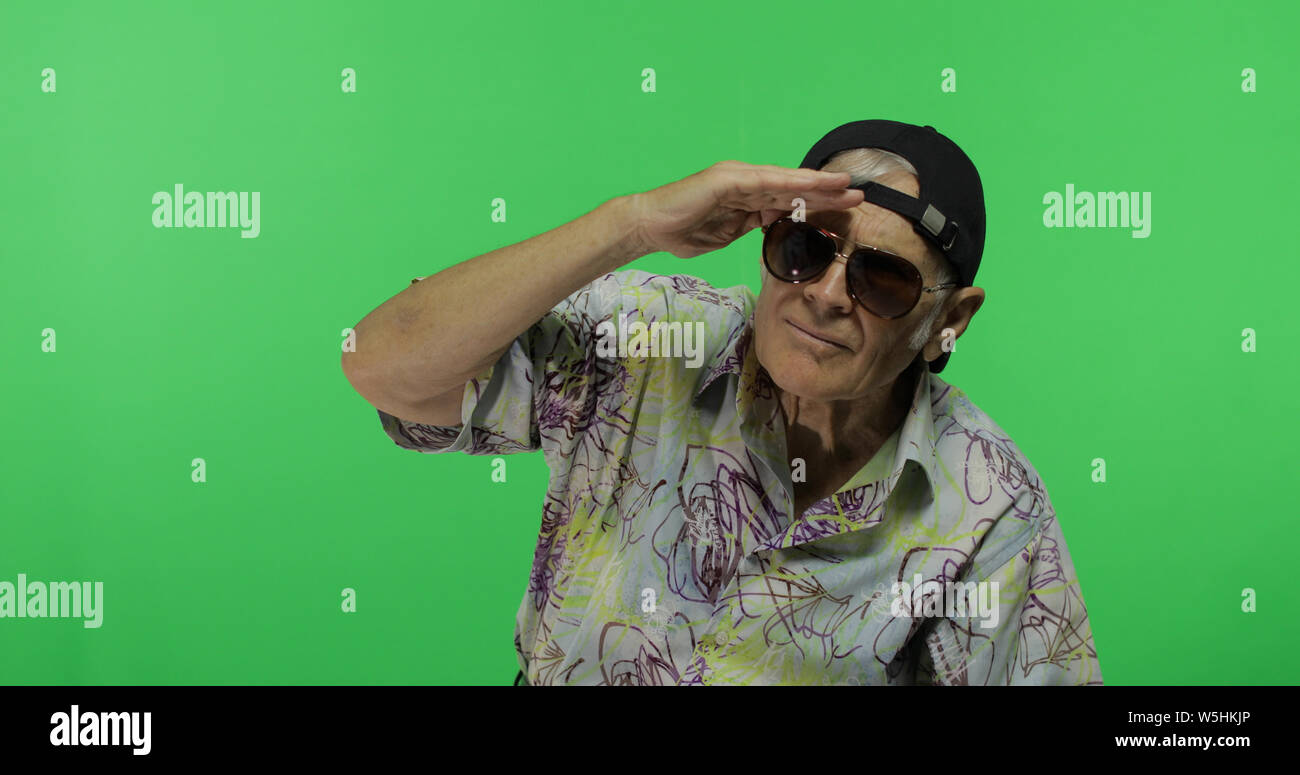 El hombre superior turista gafas de sol mirando algo. Viejo hombre en chroma key de fondo. Ancianos abuelo en camisa colorida. Lugar para su logotipo o texto. Fondo pantalla