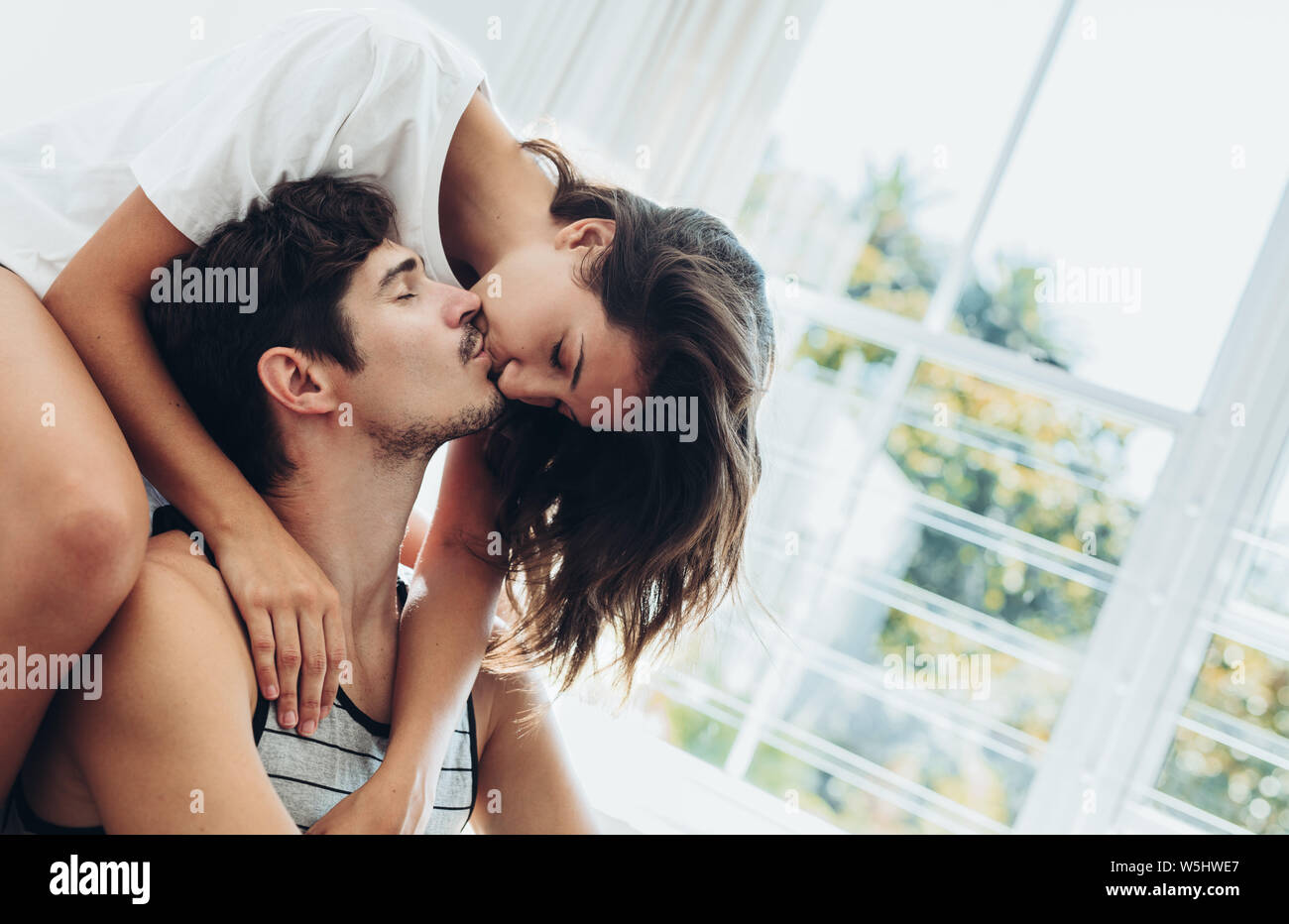 Pareja compartiendo un apasionado beso. Mujer sentada en la cama besando a  su novio en casa Fotografía de stock - Alamy