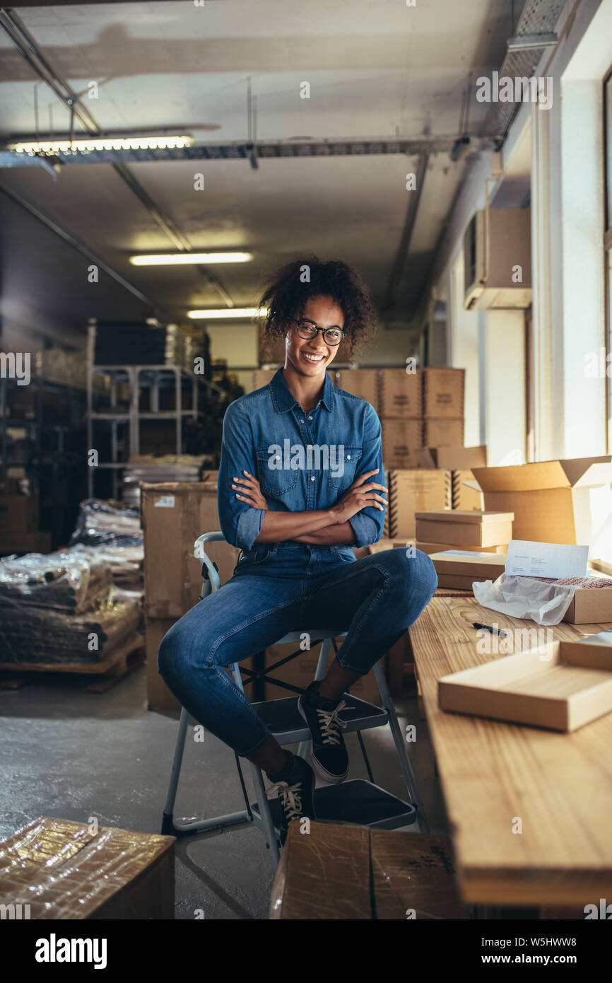 Mujer sonriente sentado en el escritorio con cuadros alrededor de paquetería. Emprendedor femenino de una tienda de venta online. Foto de stock